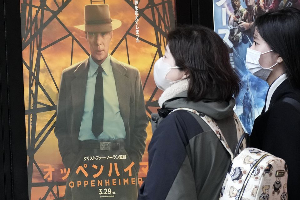 People walk by a poster to promote the movie Oppenheimer (Eugene Hoshiko/AP)