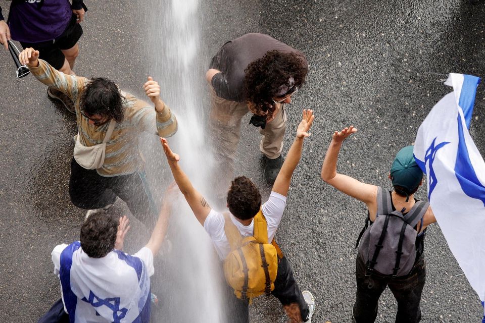 People gesture as police use water cannon as demonstrators block a road in Tel Aviv. Photo: Amir Cohen