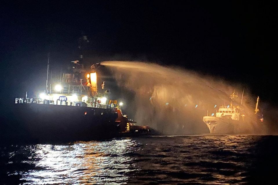 A firefighting-equipped tug boat, left, contacted by the Malta Vessel Traffic Services (VTS) helps controlling a fire occurred on the bow of the Conscience vessel in international waters of the Mediterranean Sea. (Malta Vessel Traffic Services via AP)