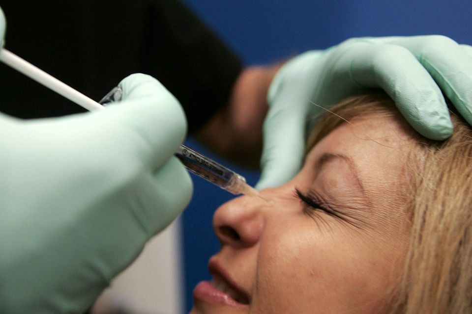 A doctor injects botox into smile wrinkles on the bridge of a patient's nose.